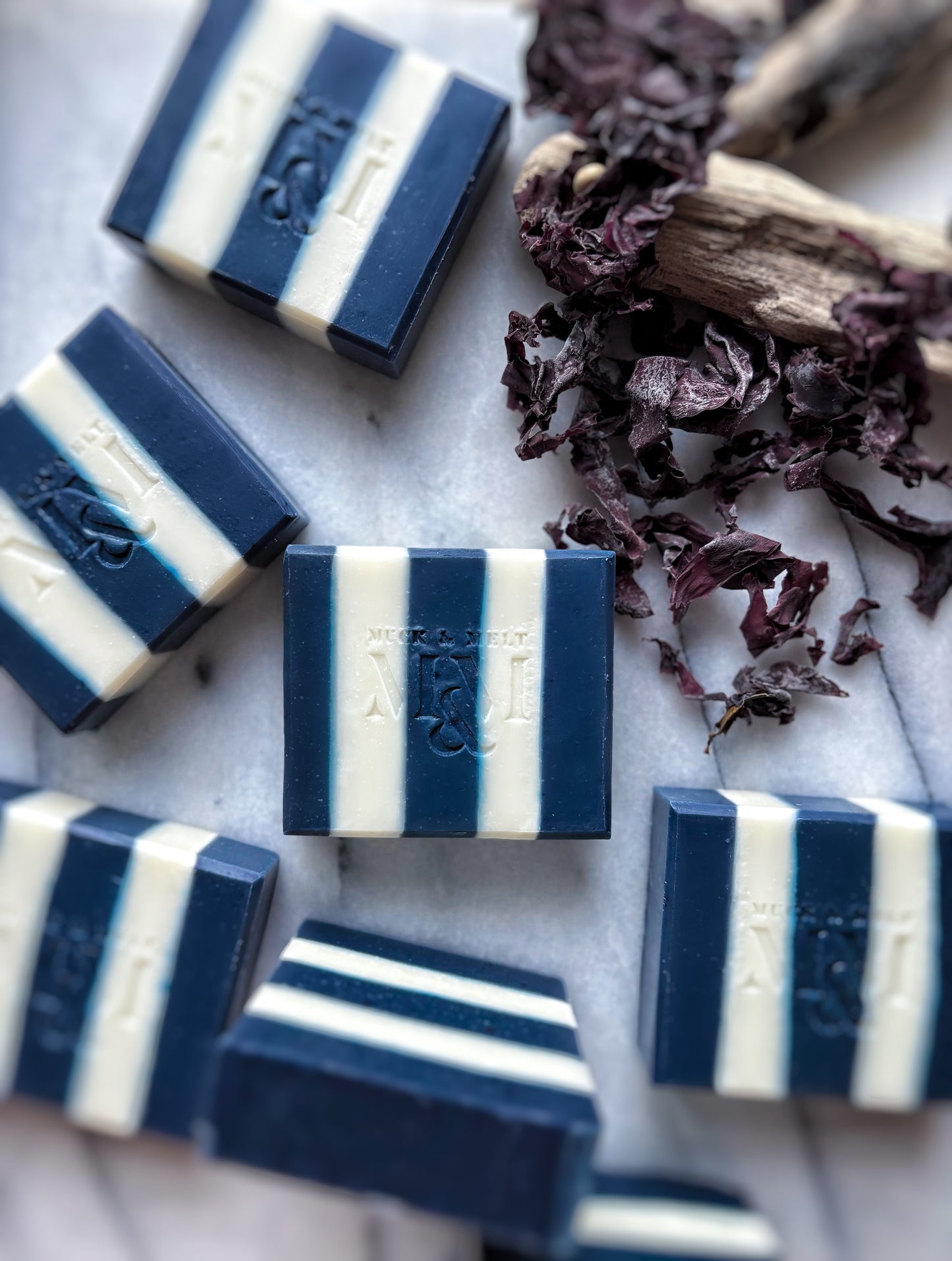 Blue and white striped soap bars on a marble surface with dried seaweed.
