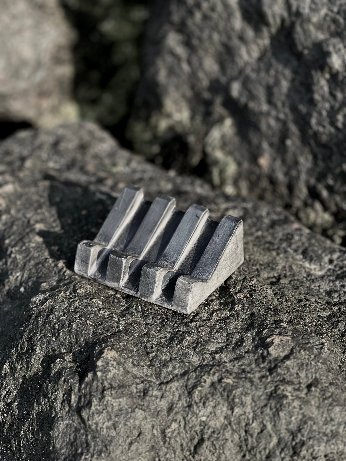 Black soap dish with organic design and slotted lines for drainage pictured on rocks