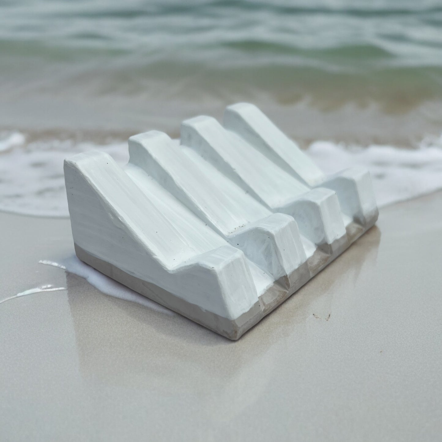 Organic-shaped soap dish with natural clay texture and rustic feel on beach with ocean behind
