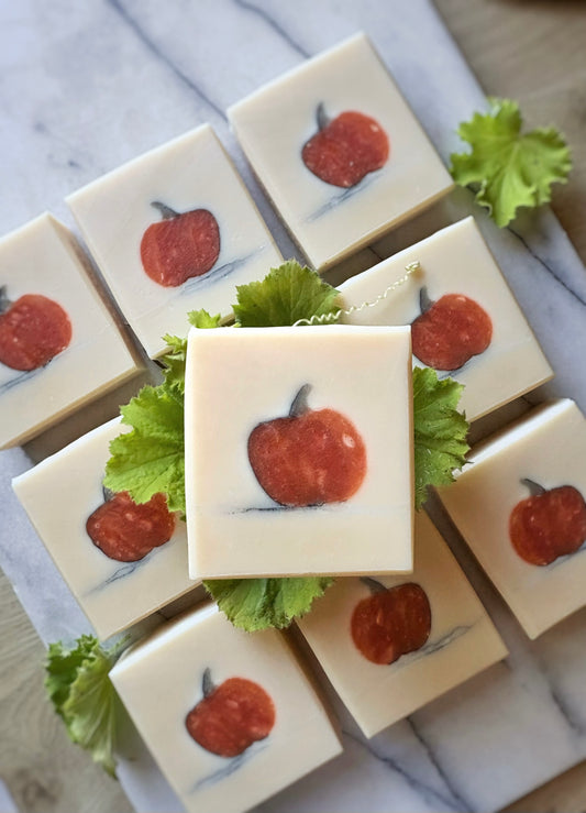 Square white soap bars arranged on a marble surface, each with a pumpkin illustration, with green leaves placed around.