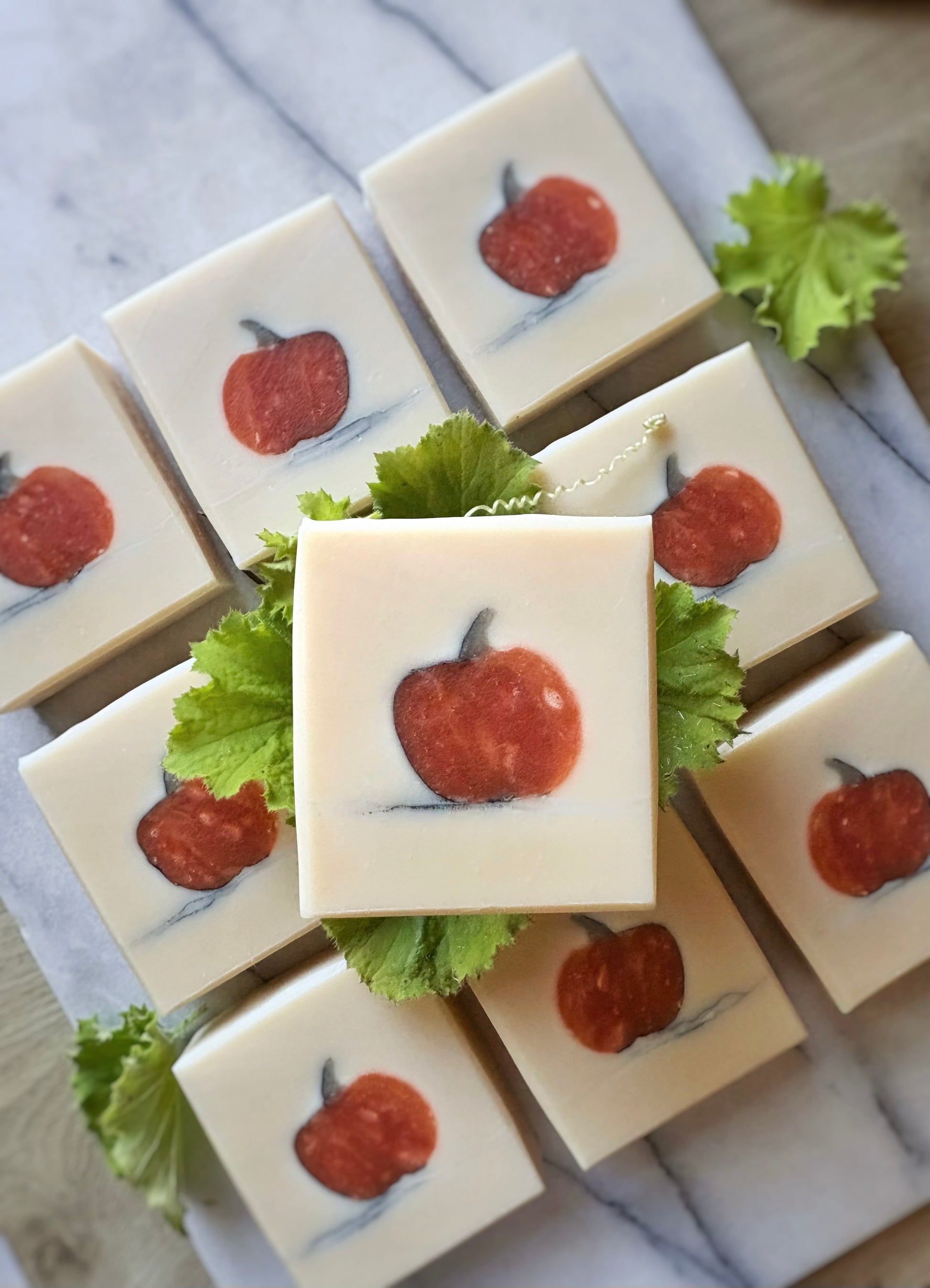Square white soap bars arranged on a marble surface, each with a pumpkin image with green leaves placed around them.