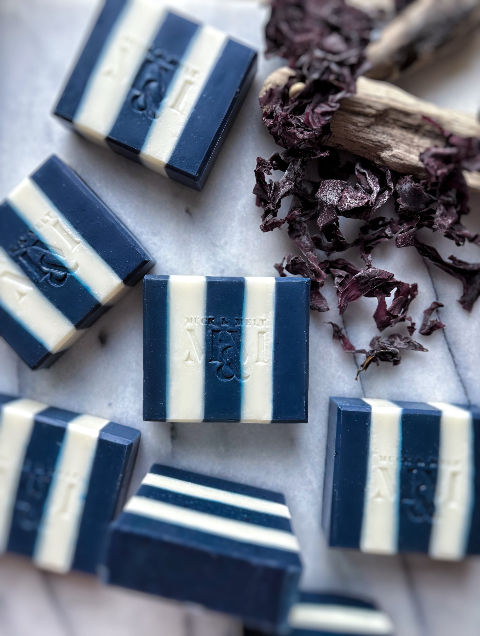 Blue and white striped soap bars on a marble surface with dried seaweed.
