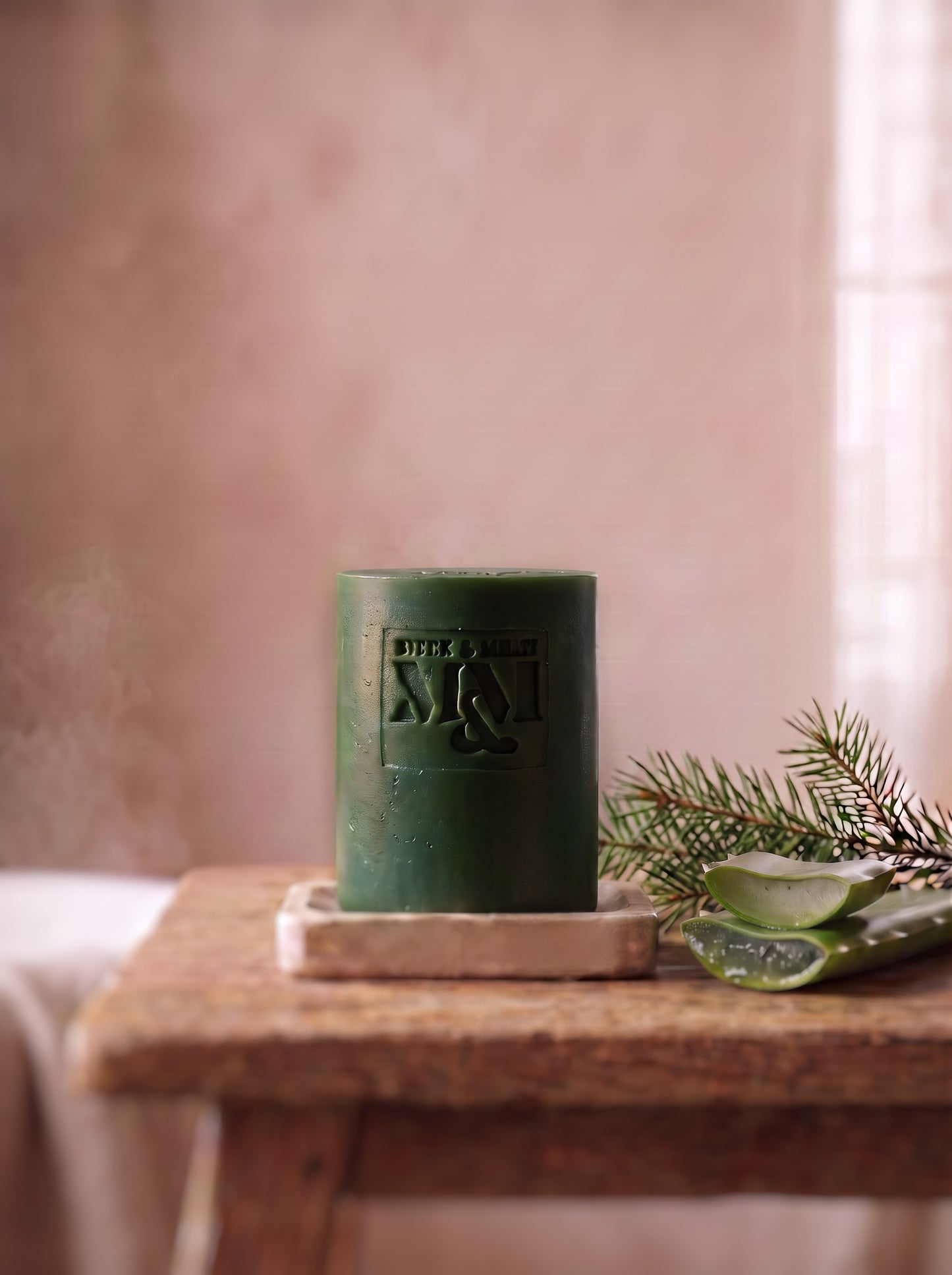 a dark green soap on a rustic table with a branch of fir and some aloe vera