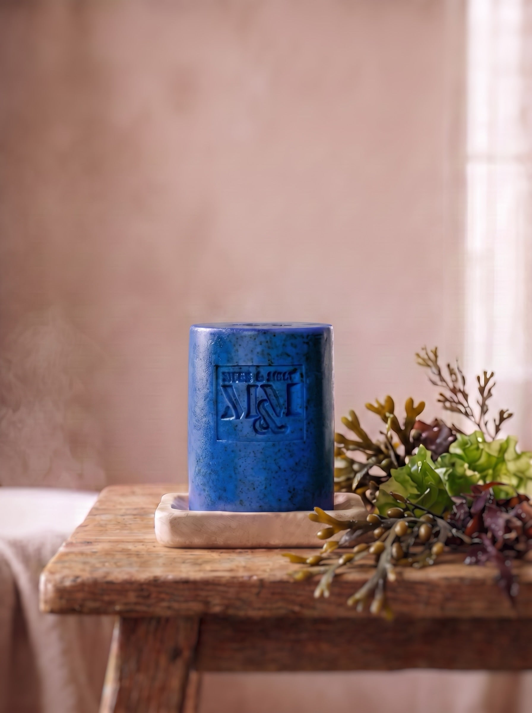 a naturally coloured blue soap sits in a dish with seaweed.