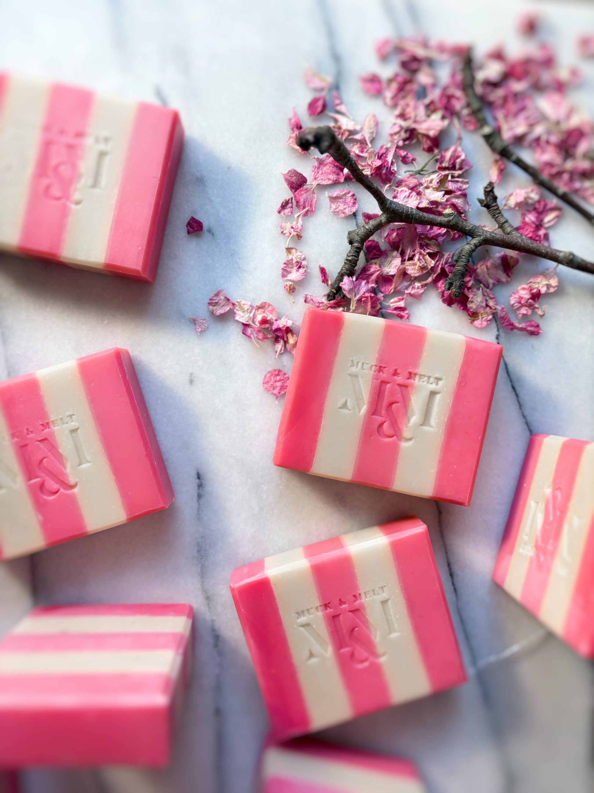 Pink and white striped soap bars with a brand logo on a marble surface with cherry blossoms. Perfect Valentines day gift for her.