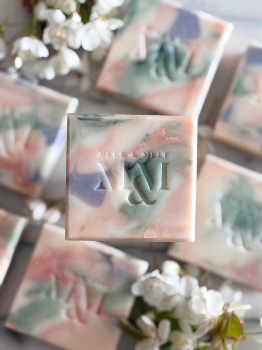 natural Artisan soap bar with floral-inspired swirls in natural pink, green, lilac and white hues with blossom flowers close up
